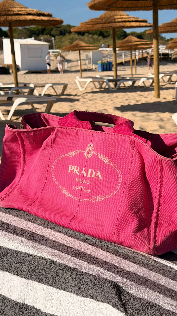 Pink Prada bag on a beach with umbrellas and sand in the background